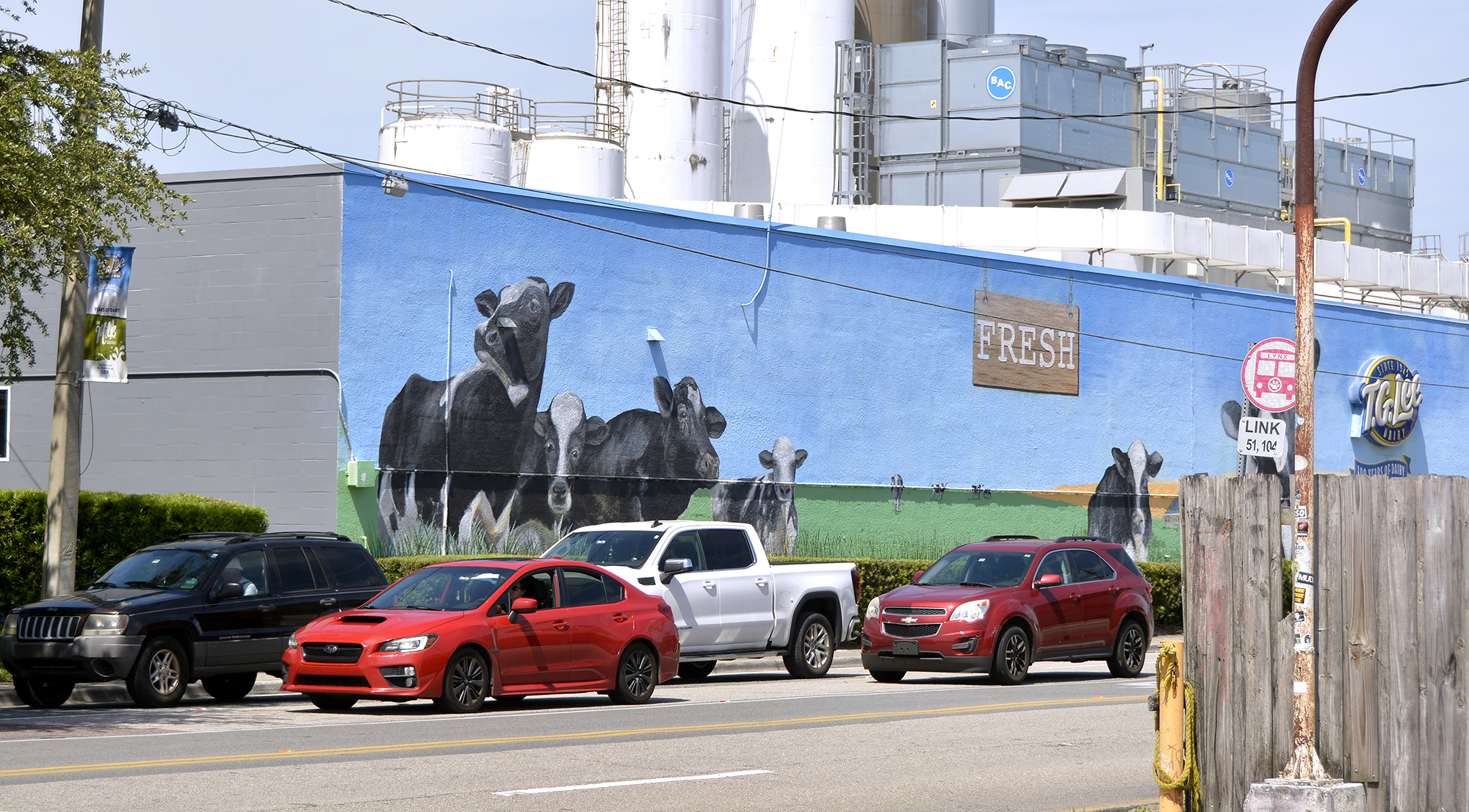 A row of cars in front of a cow pasture mural in the Milk District.